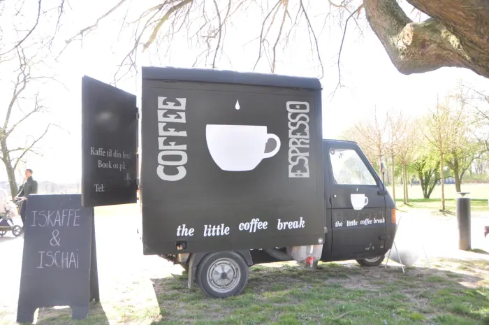 Sort kaffevogn fra The Little Coffee Break parkeret på græsset under et træ i solskin